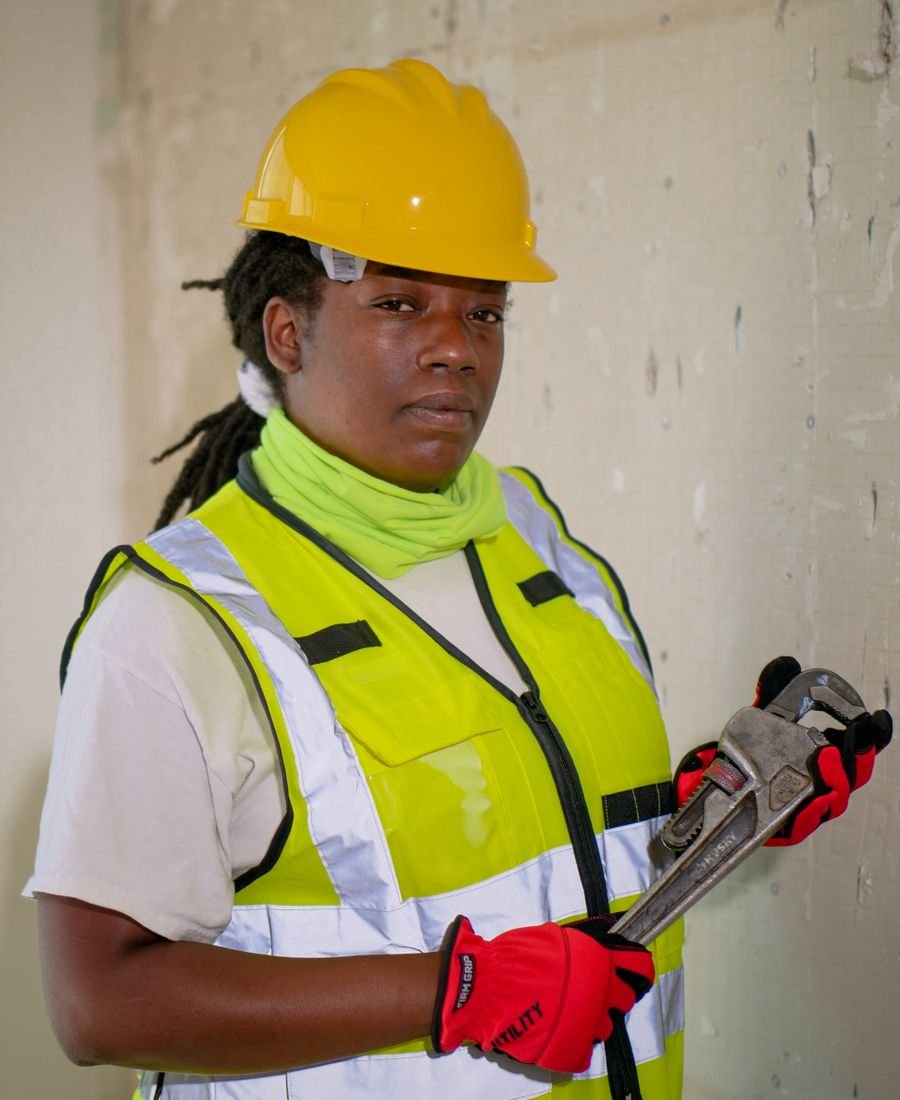 Tradesperson in high-visibility clothing and safety gear holding a pipe wrench